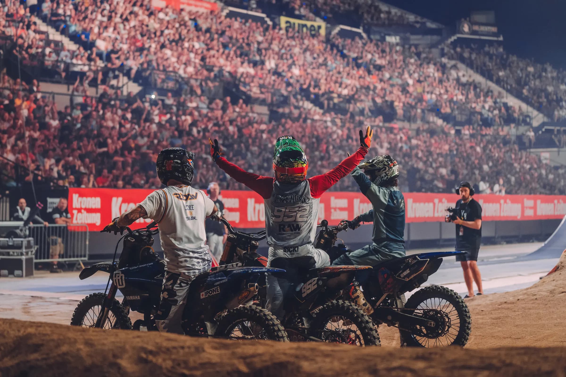 Three riders celebrating in front of packed stands